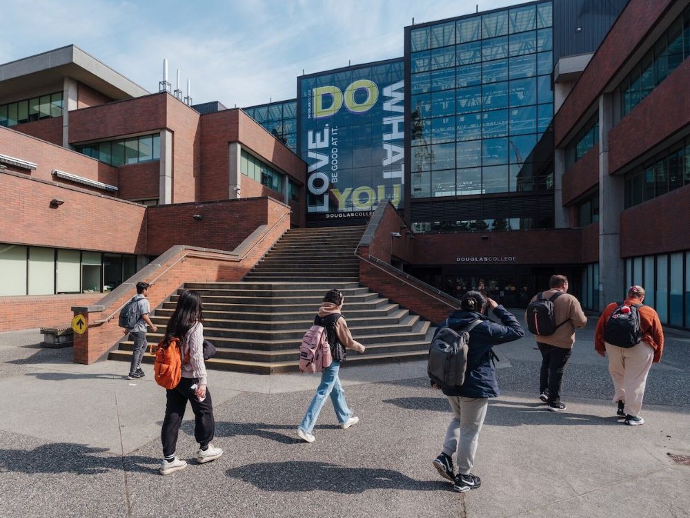 A college campus with modern red brick buildings and students walking in front of buildings.
