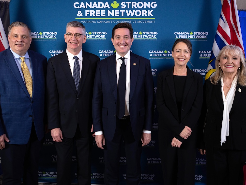 Five people in suits &mdash; three men on the left, two women on the right &mdash; stand together, smiling at the camera.