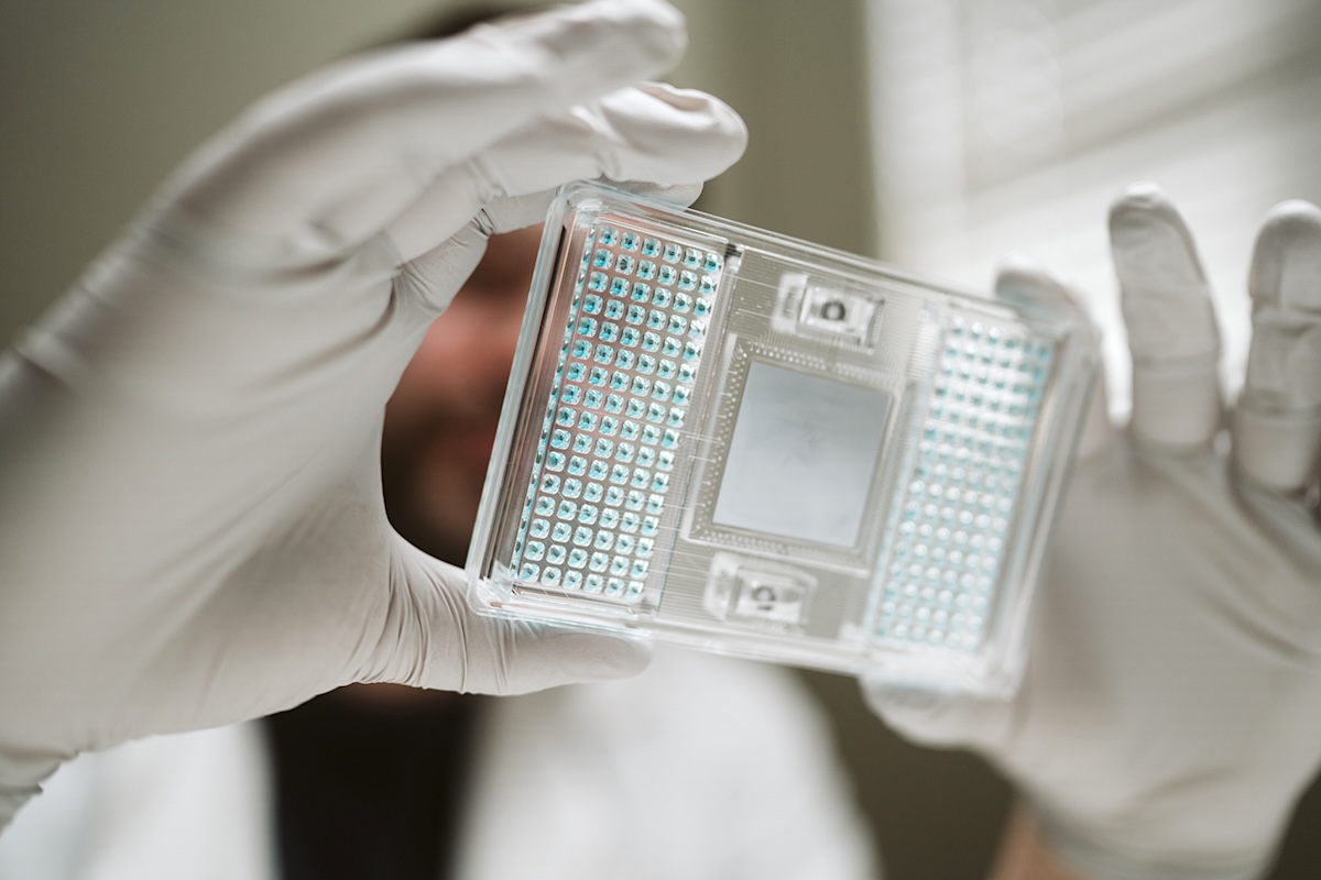 A man with white gloves holds up a clear rectangle with dozens of pale blue dots on it. 