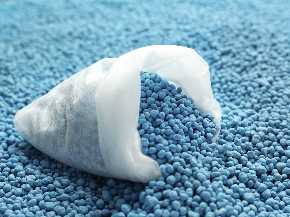 A tipped-over white bag spills blue pellets onto a flat surface covered in the same type of pellets.