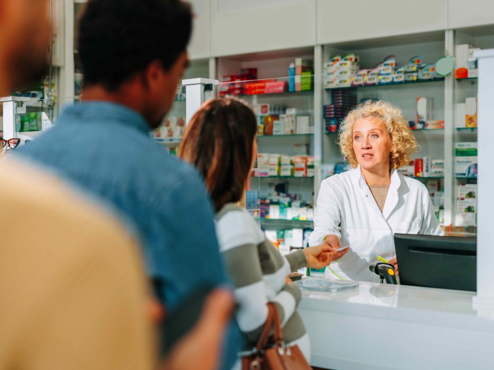 A line of three people wait in front of a pharmacy counter.