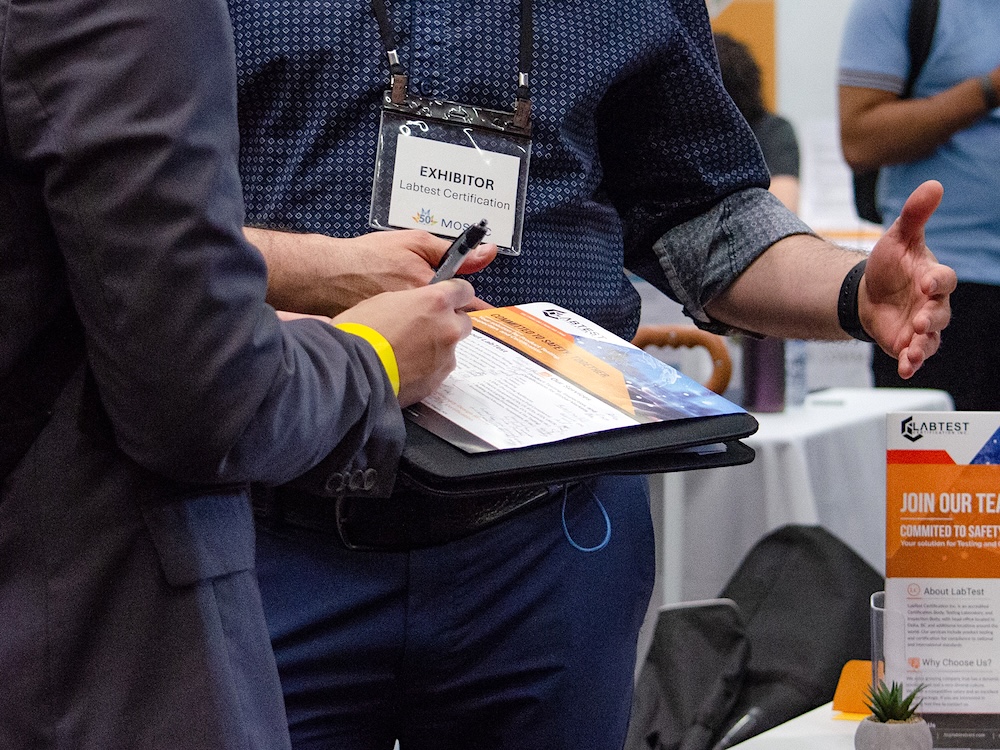 A close-up of two people&rsquo;s hands and arms as they hold a folder and exchange business cards.