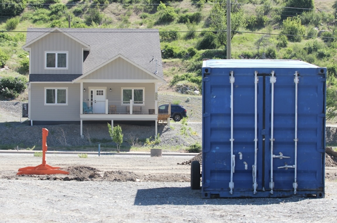 A rebuilt house is surrounded by gravel and a blue sea can.