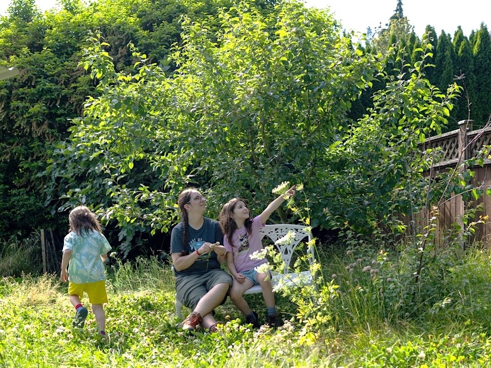 A woman and two young kids in a greenery-filled yard.