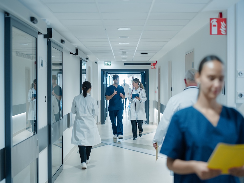 Health-care workers walk down a busy hallway in a hospital. 