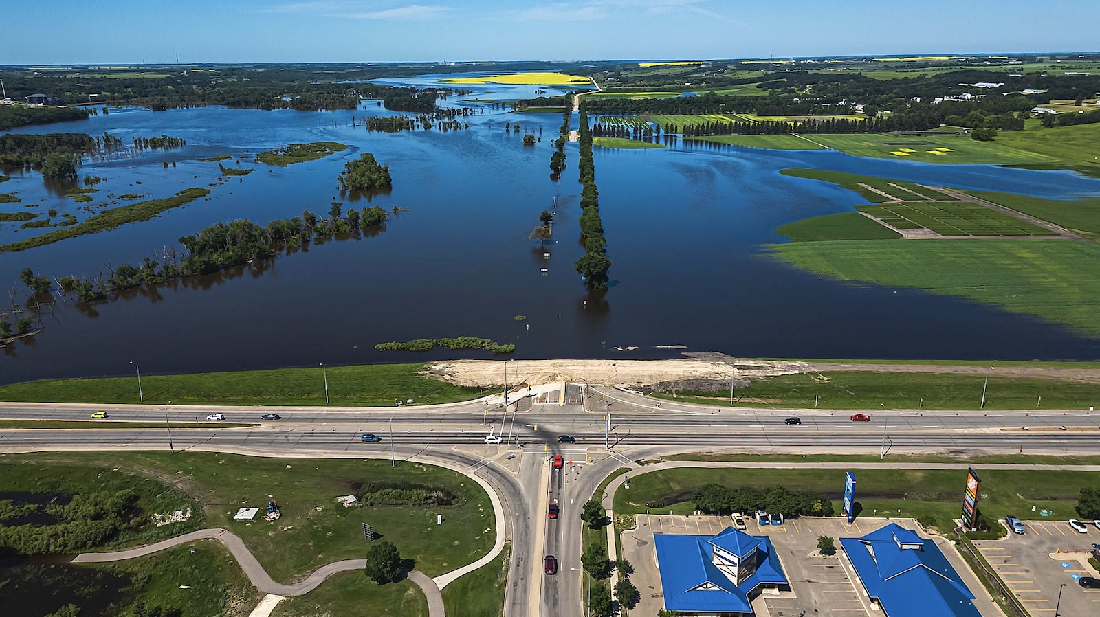 An aerial view of a highway interchange with flooded prairie farmland behind it.