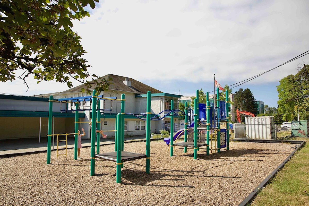 An elementary school playground features playground equipment with green railing. 