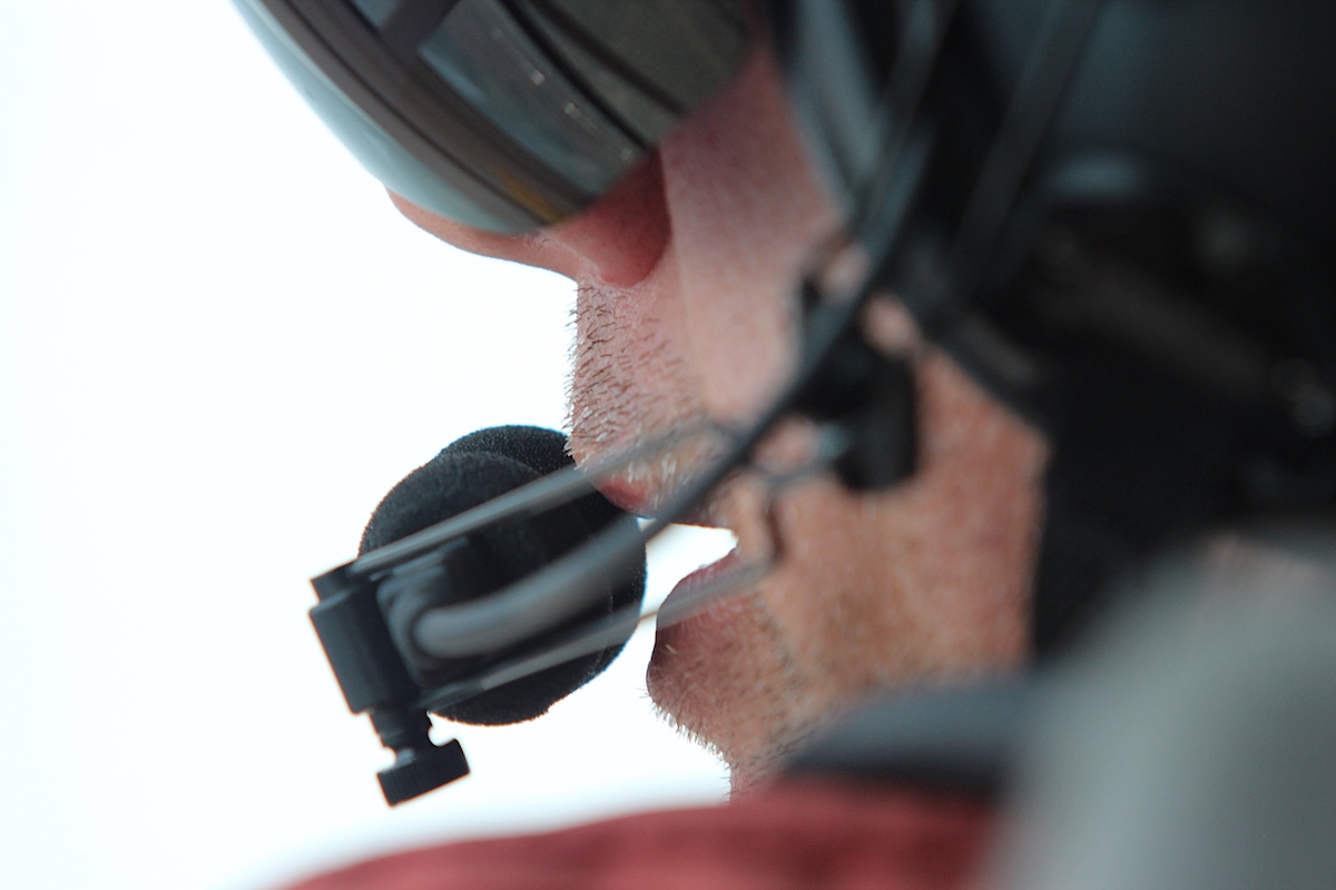 A man wearing a pilot&rsquo;s helmet and shield speaks into a headset.