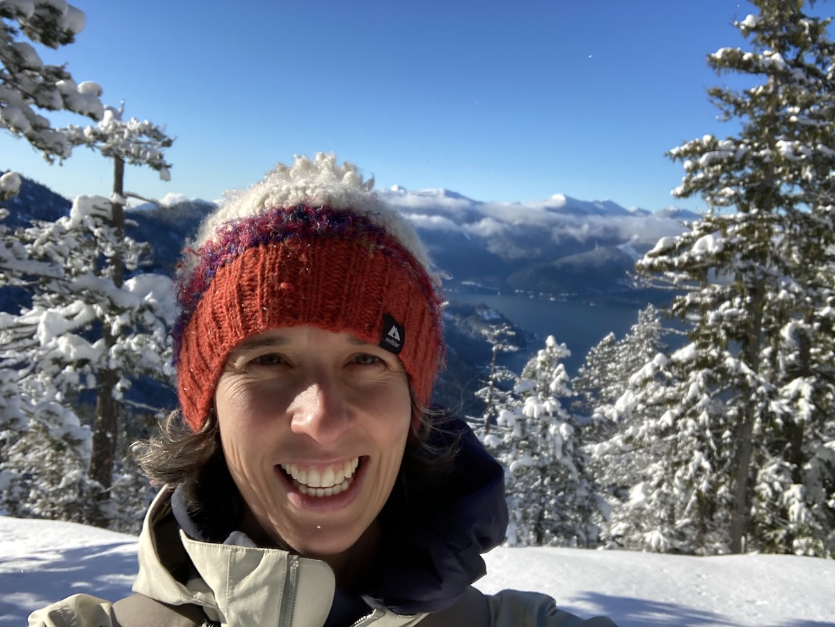 A woman with light skin tone wearing a toque, in a snowy mountain setting.