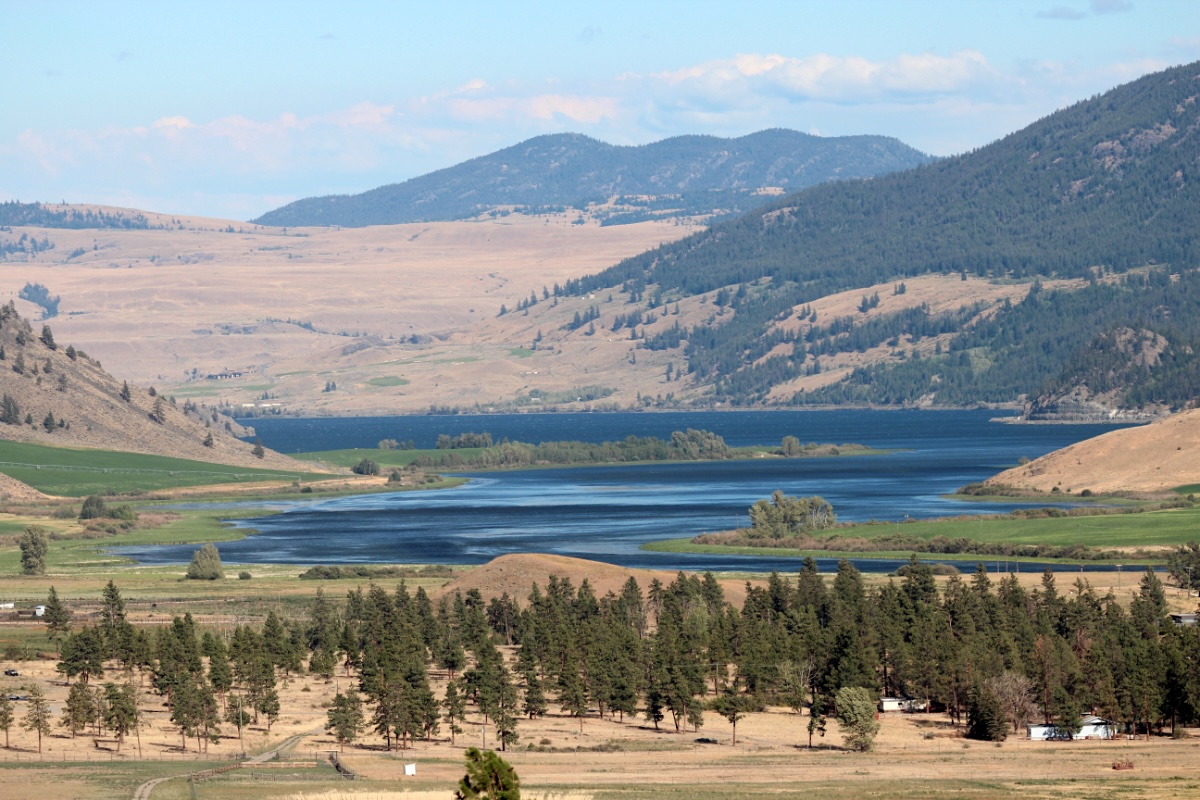 A blue lake with greenery on the shores sits in the basin of an arid valley with brown hillsides.