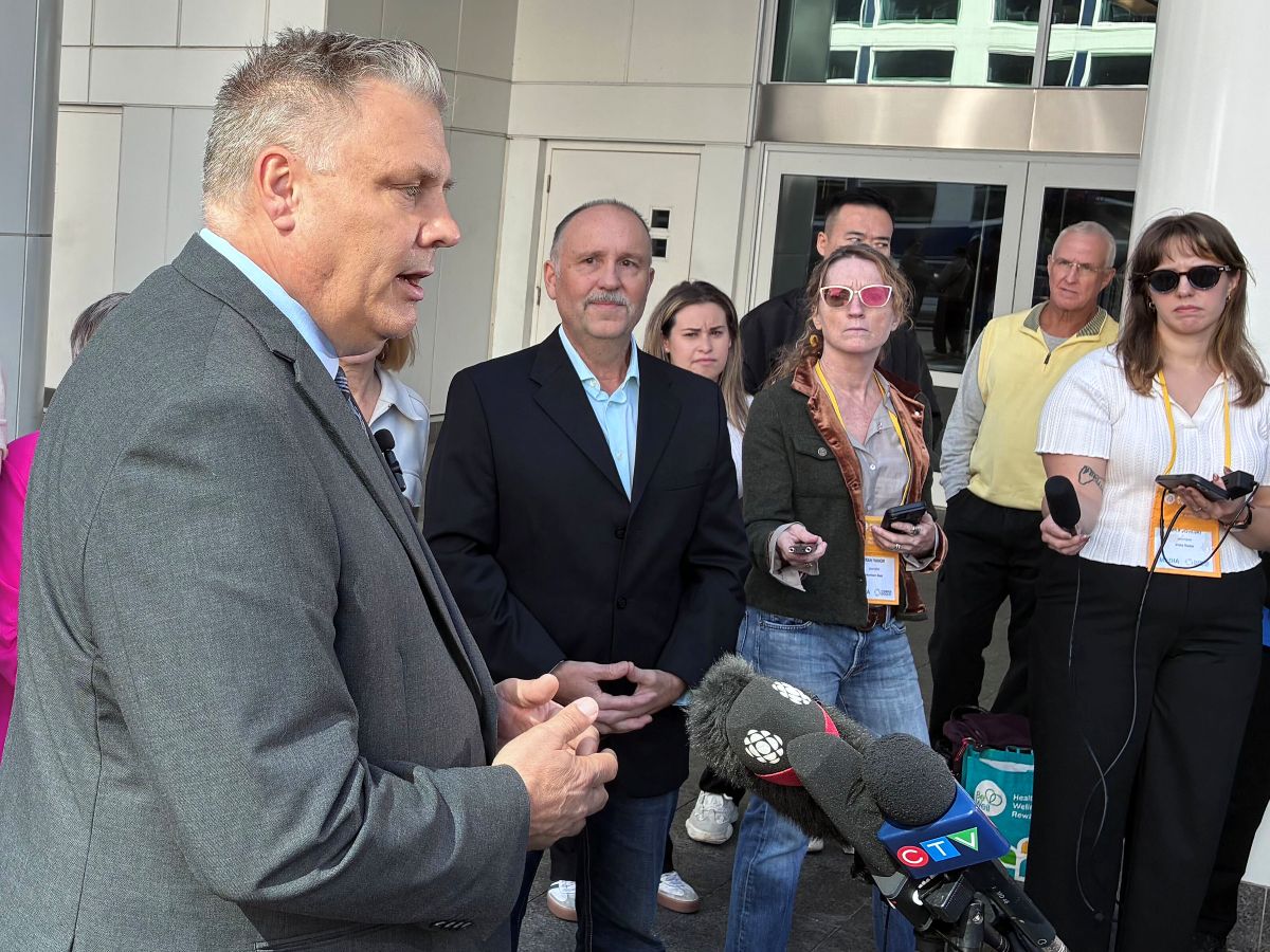 Peter Milobar speaks into microphones, while reporters and other politicians look on.