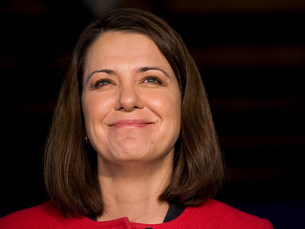 Danielle Smith, a brown-haired white woman in a red jacket, smiles.