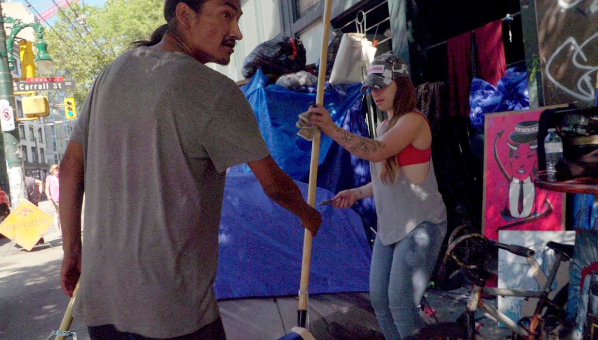 Aaron hands a broom to an unidentified woman on his right, on Carrall Street in Vancouver&rsquo;s Downtown Eastside. 