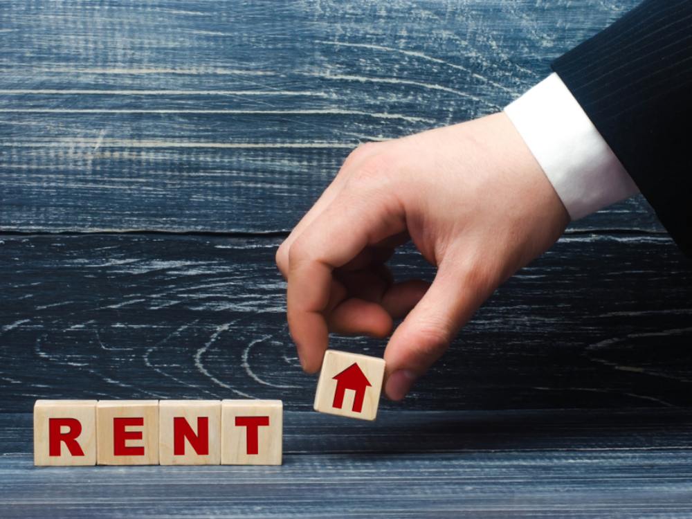 The arm of a man wearing a suit picks up a wooden piece with a symbol of a home, which had finished a series of pieces spelling out &lsquo;rent.&rsquo;
