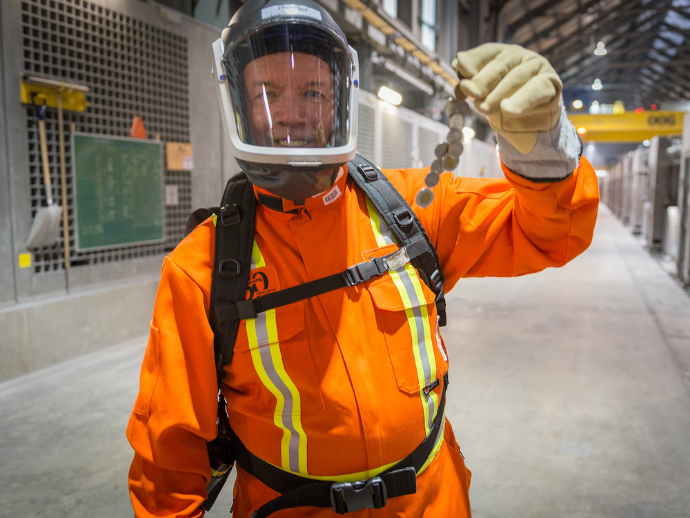 Former premier John Horgan wears an orange protective suit, a helmet and a face mask.