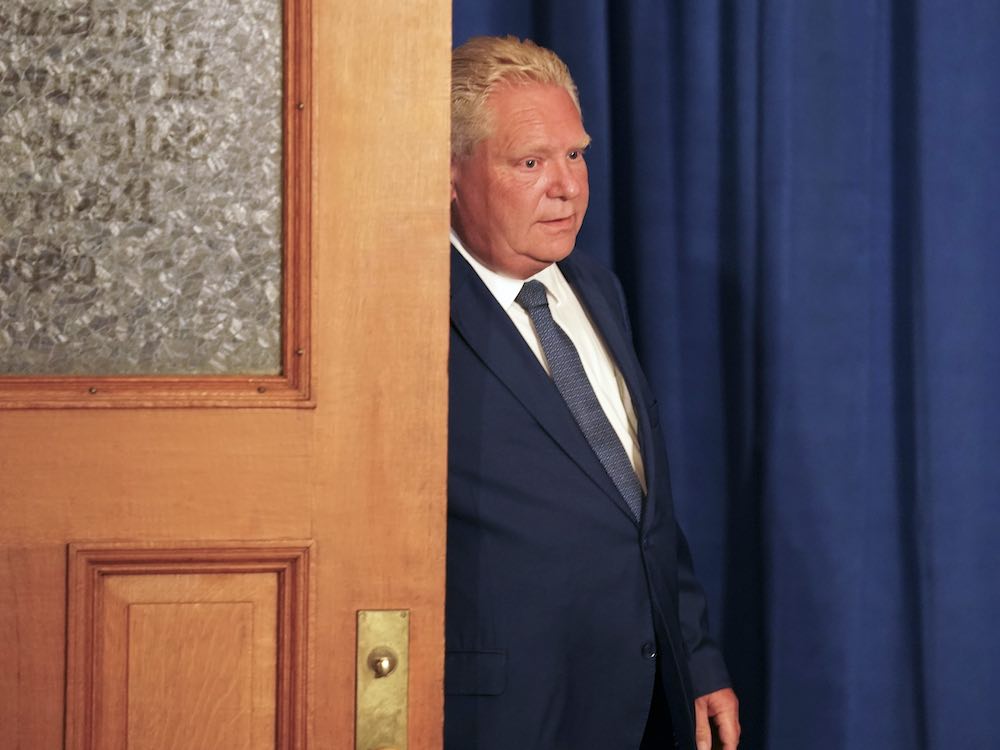 Ontario Premier Doug Ford, in a blue suit and tie, beside a brown door.