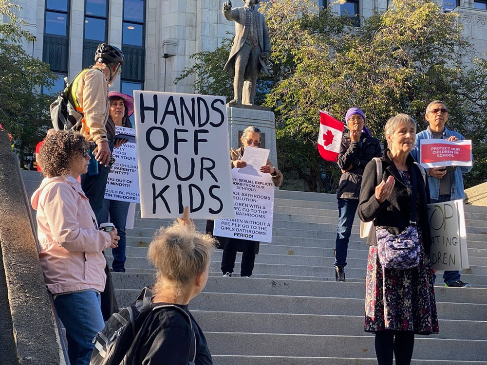 A small crowd holding placards and Canadian flags gathers on the steps at city hall in Vancouver.