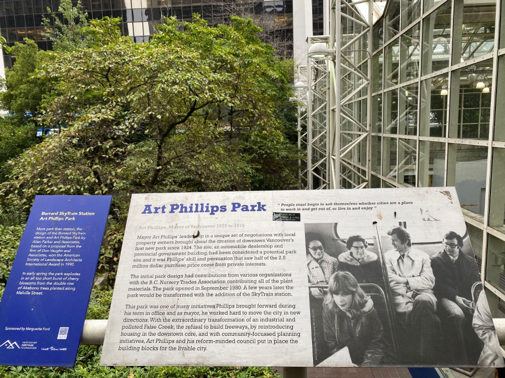 A plaque titled &ldquo;Art Phillips Park&rdquo; with text and a photo in front of a small tree.