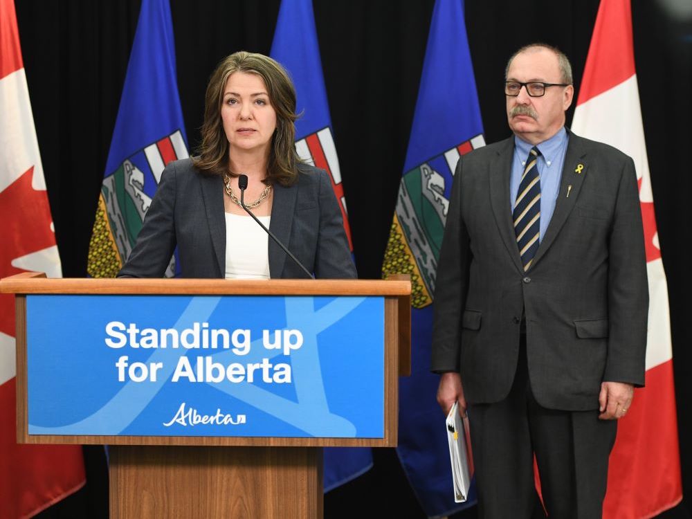 A 50-ish woman with shoulder-length dark hair wearing a blue suit stands beside a man of similar age wearing a dark grey suit.