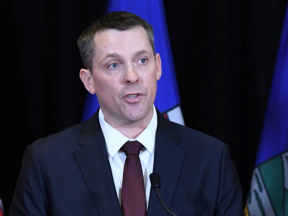 A man in his early 40s, with short dark hair and wearing a blue suit, white shirt and burgundy tie.