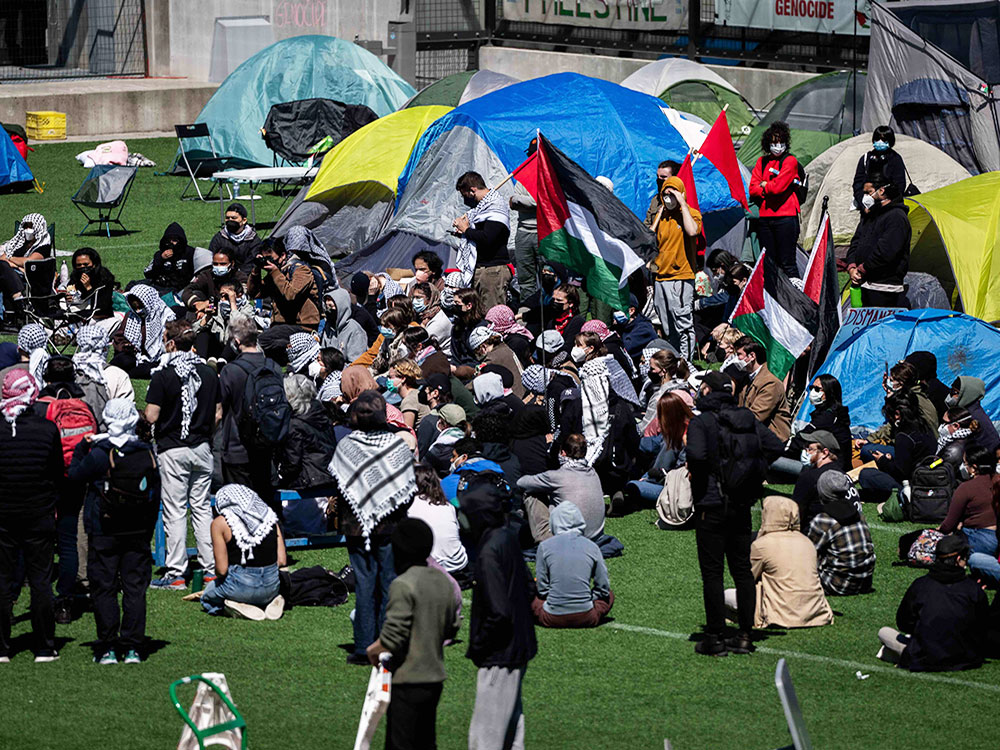 A group of about 40 people sit and stand with about a dozen tents behind them.

