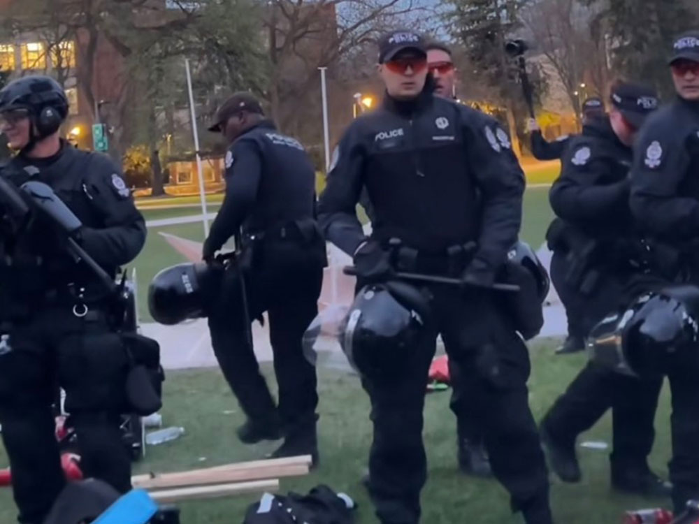 Police in black clothes, with batons and helmets, prepare to clear a camp.