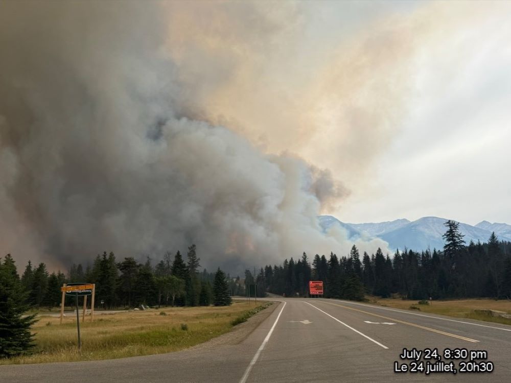 A road leads towards a huge column of grey and white smoke rising from hills.