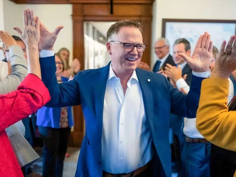 Kevin Falcon, wearing a white button-up shirt and blue suit, high-fives supporters.