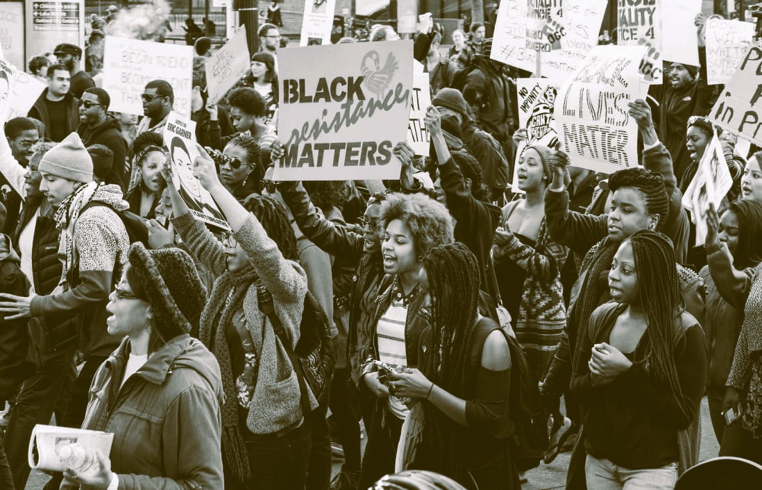 Marching protesters, mostly young and Black and smiling, hold up signs including one saying 'Black Resistance Matters.'