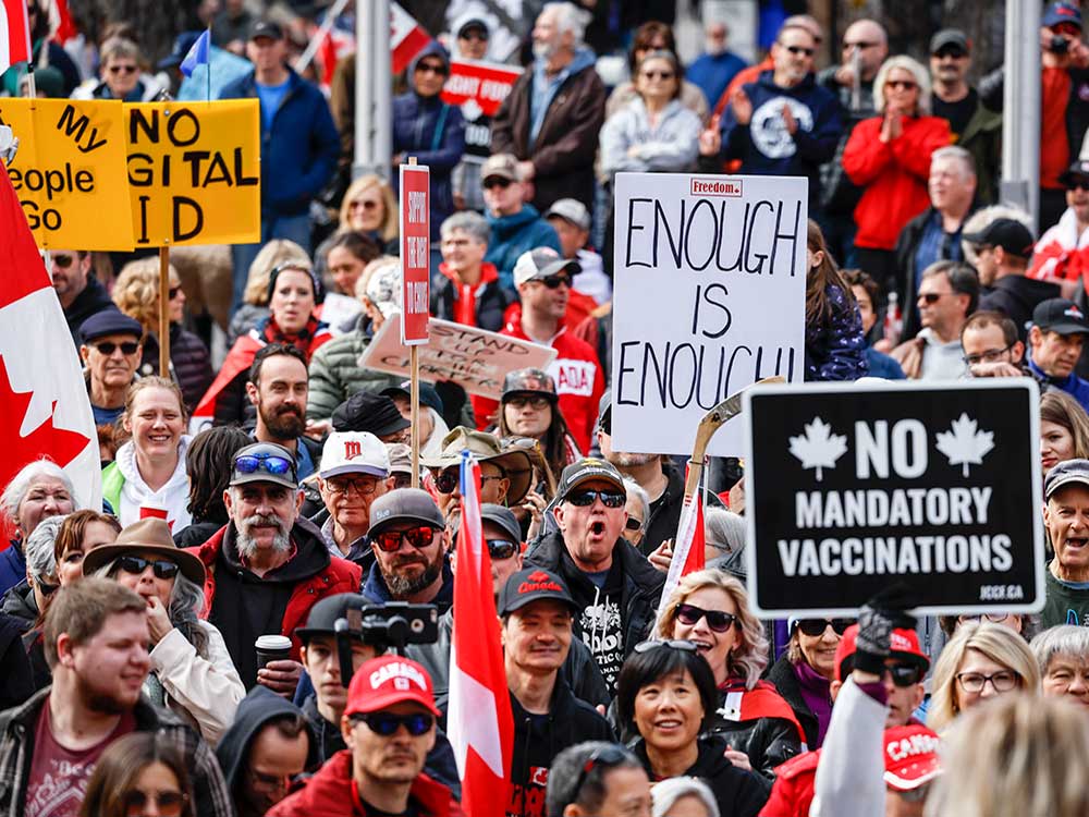 A large crowd of people in the street. Some carrying signs saying, “No digital ID” and “No mandatory vaccinations.”