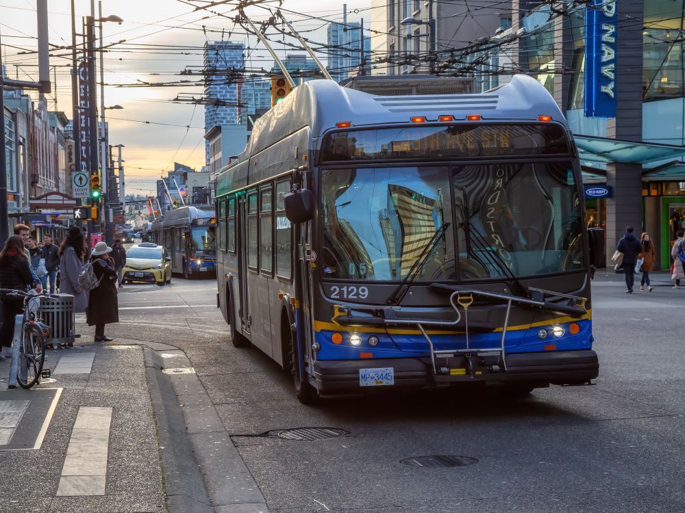A bus drives along Granville Street in downtown Vancouver as pedestrians on the sidewalks look on.
