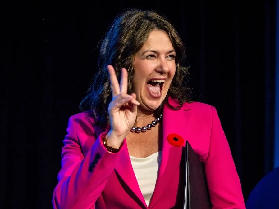 A middle-aged woman with shoulder-length dark hair smiles and gives a V for victory sign.