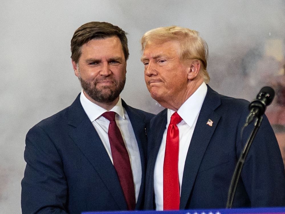 Two light-skinned men, one 40 and one 78, stand close together. They are wearing blue suits, white shirts and reddish ties.