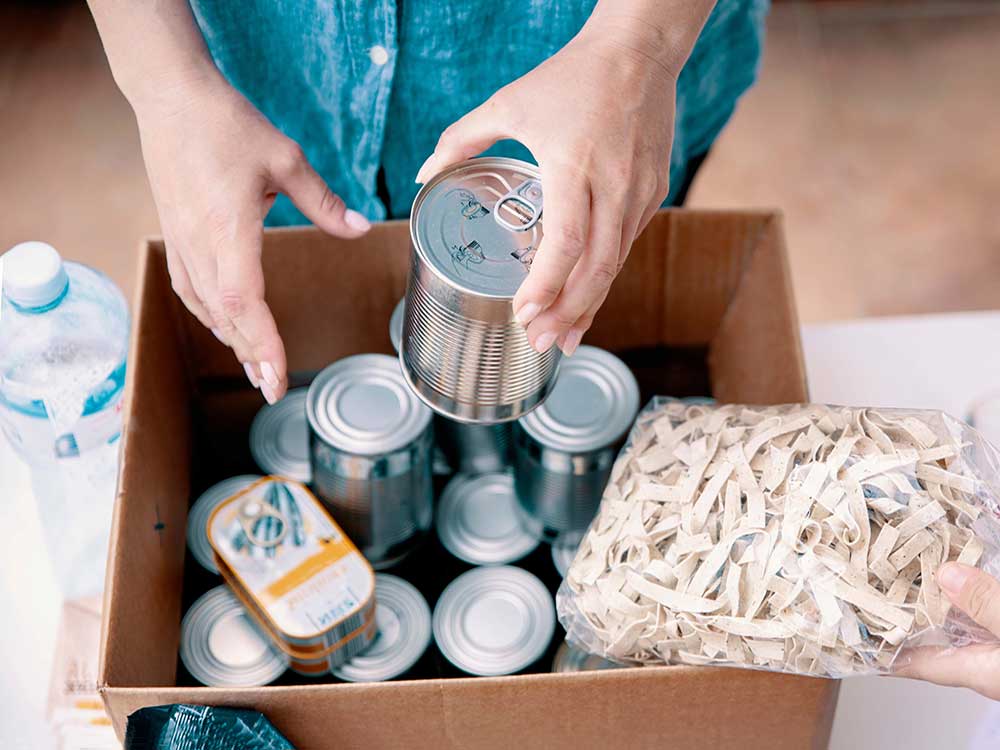 Hands place food items in a cardboard box.