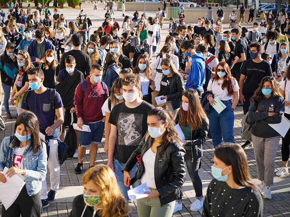Dozens of people of university age are in an open space, all wearing masks.