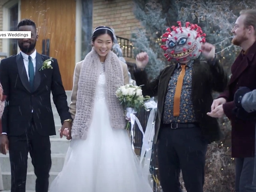 A couple leave a building after being married. Among the guests is a person with a large COVID virus as a head.
