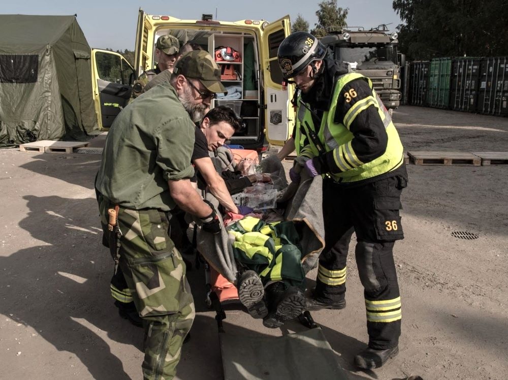 Four people in uniform lift a person from a stretcher.
