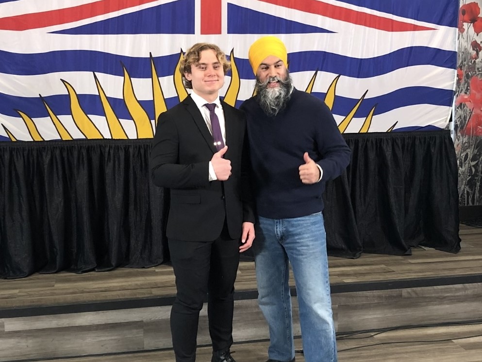 An 18-year-old light-skinned man in a suit beside an older man wearing a turban, sweater and jeans. Both are making a thumbs-up gesture.