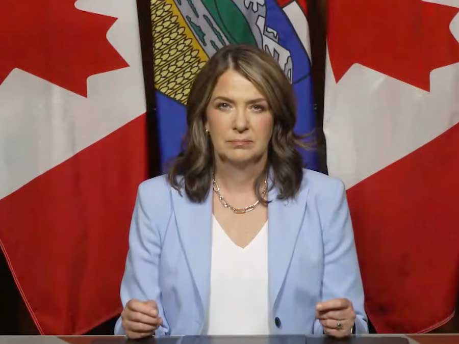 Danielle Smith, a middle-aged light-skinned woman with brown hair, sits at a desk and looks at the camera.