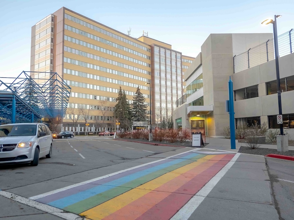The exterior of a series of beige medical buildings on a clear day at dusk. A rainbow sidewalk is in the foreground.