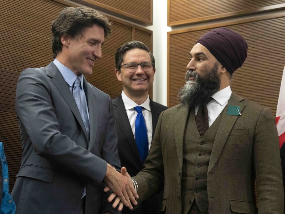 Justin Trudeau, a 53-year-old light-skinned man, shakes hands with Jagmeet Singh, a 46-year-old Indo-Canadian man wearing a turban. Pierre Poilievre, also 46, looks on from behind.