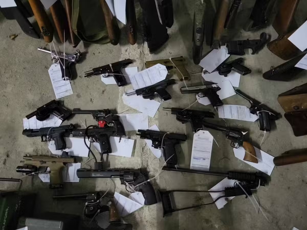 A large selection of guns, with evidence tags, is displayed.