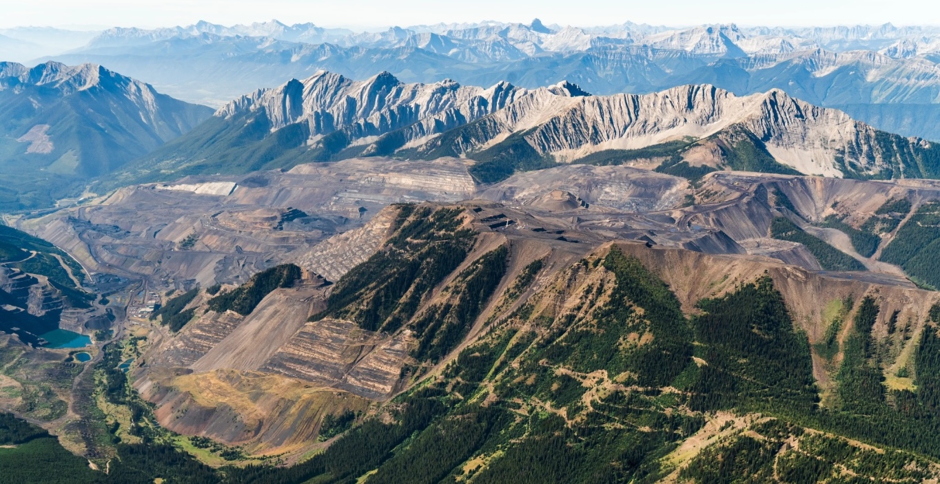 A large, dark coal mine in front of a ridge of towering, rocky mountains.