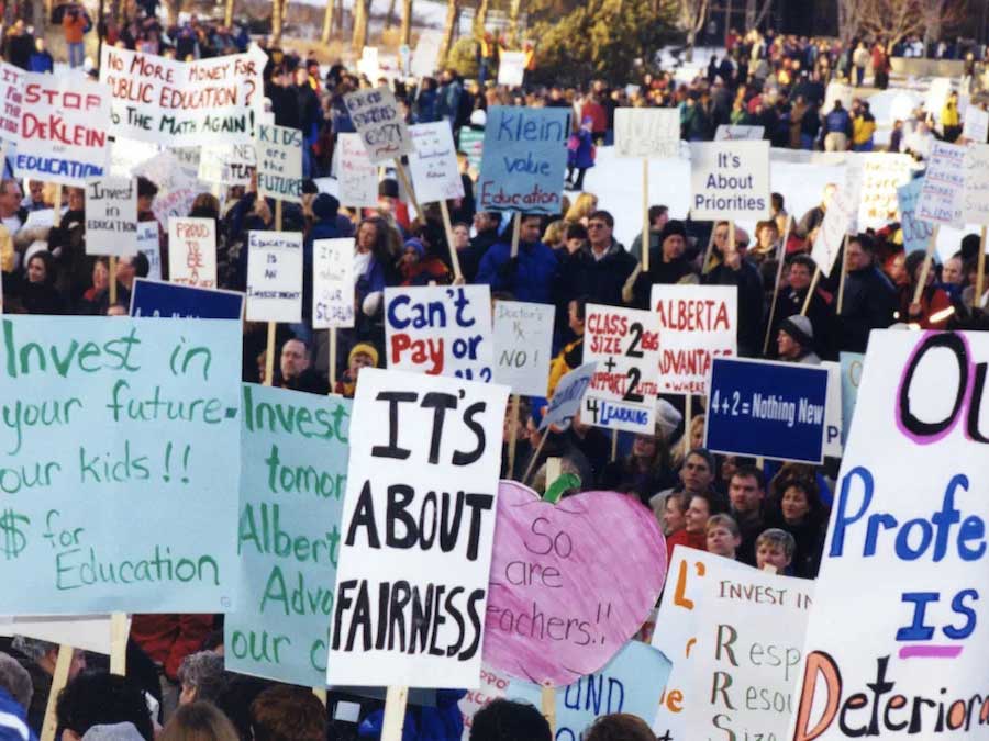 A large crowd of people holding signs gather on a winter day.