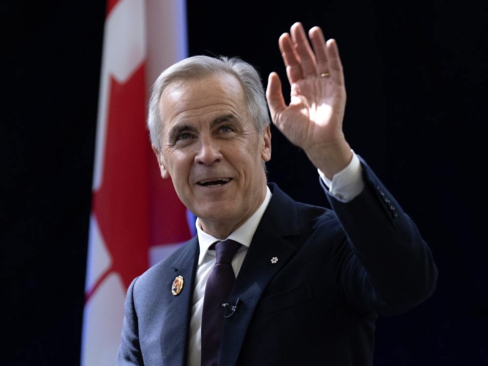 Mark Carney, a 60-year-old light-skinned man with grey hair in a dark suit, white shirt and tie, waves.