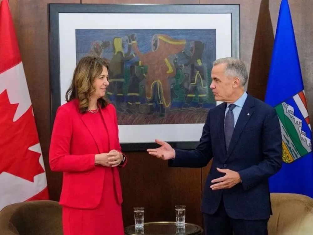 Danielle Smith and Mark Carney are standing in an office with flags in the background.