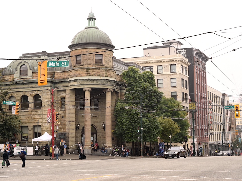 A sandstone building, the Carnegie Community Centre, at a busy intersection in Vancouver&rsquo;s Downtown Eastside neighbourhood.