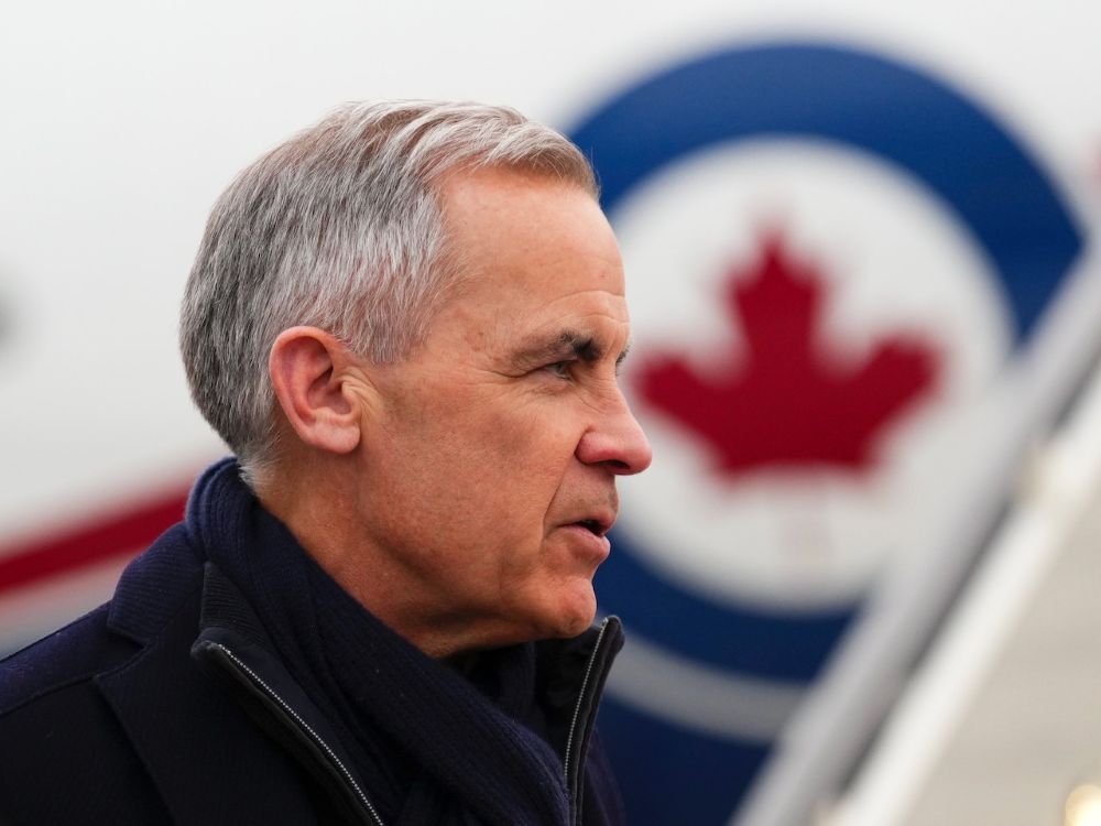 A man in his 60s with gray hair stands before a plane. He wears a black coat and the photo shows his face in profile. In the background, the RCAF logo of a red maple leaf inside a blue circle can be seen on the side of the plane.