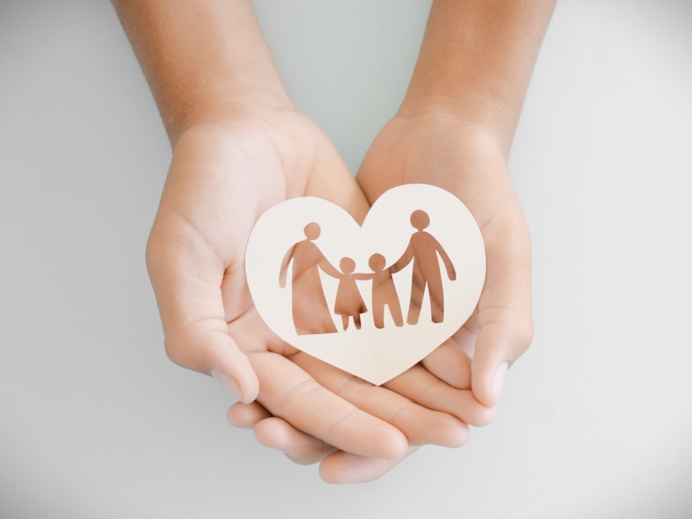 An image shows a pair of hands holding a paper heart with a cutout image of what appears to be two parents and two children.