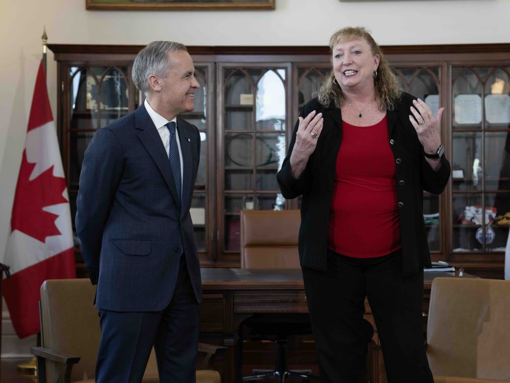 Mark Carney, a 61-year-old man in a suit, smiles at Marilyn Gladu, a 64-year-old woman with shoulder length hair and wearing a red shirt and black jacket.